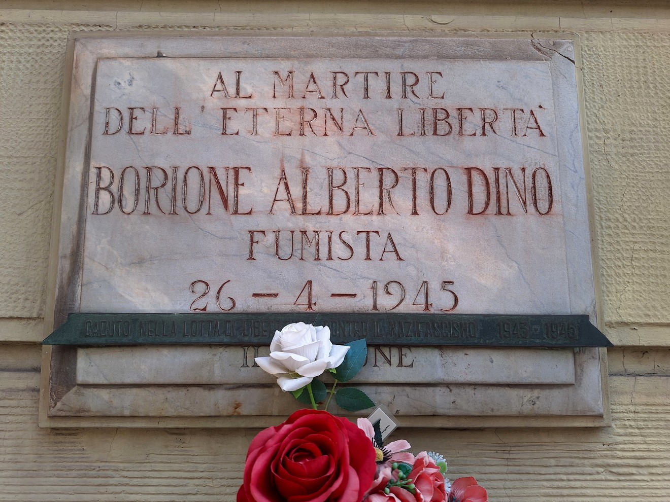 Lapide in marmo su parete esterna, con iscrizione e fiori deposti sotto, in memoria di un martire partigiano.