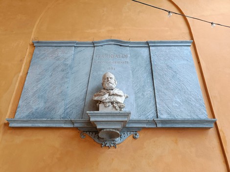 Lapide commemorativa con busto in onore dei caduti per la libertà, su sfondo arancione.