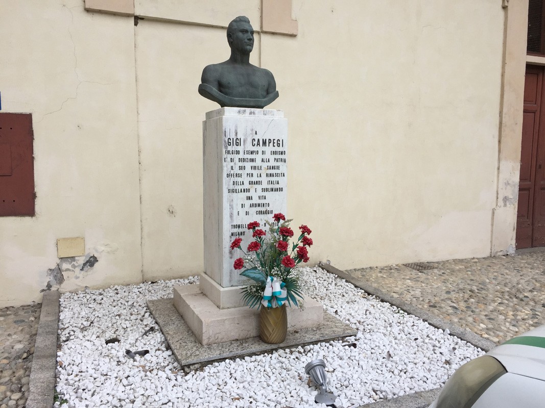 Monumento dedicato a Gigi Campegi, con busto e decorazioni floreali, ubicato in un'area storica.