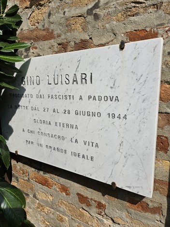 Lapide commemorativa dedicata a Gino Luisari, martire della Resistenza, affissa su muro di pietra.