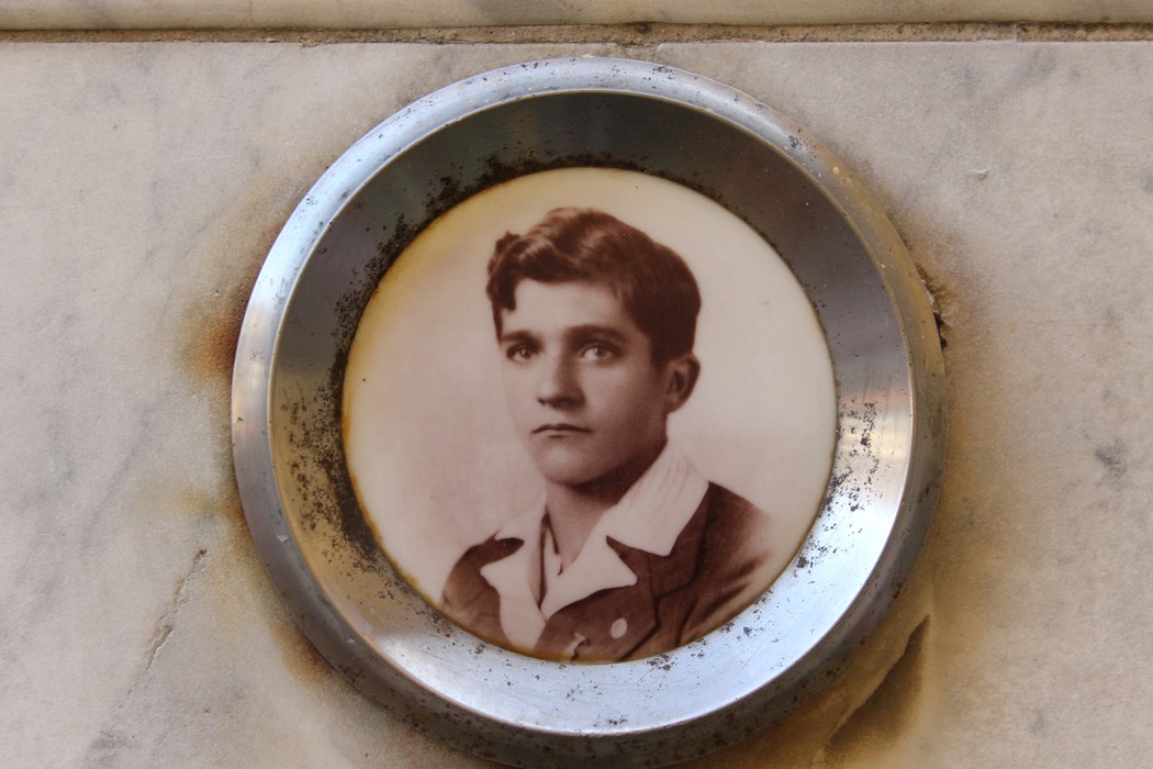 Lapide commemorativa con foto in ceramica di un giovane uomo su fondo di marmo.