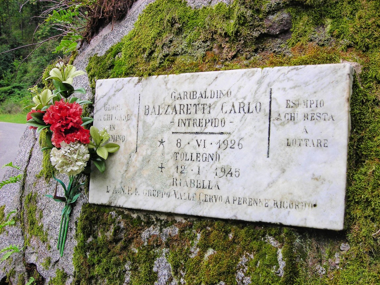Lapide commemorativa di Carlo Balzaretti, intitolata a un valoroso combattente, adornata con fiori.