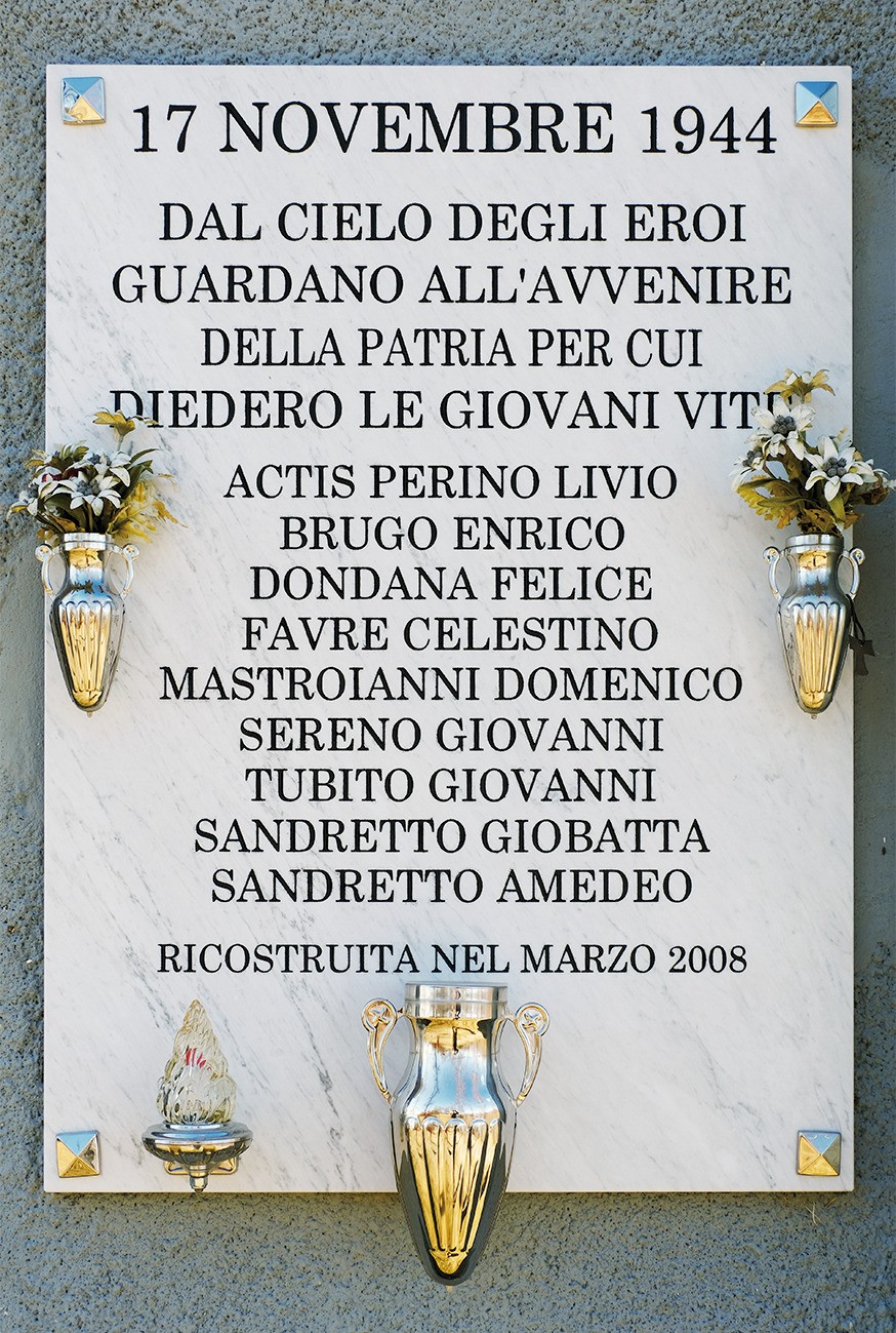 Lapide marmorea su parete, con iscrizione e due vasi dorati con fiori ai lati.