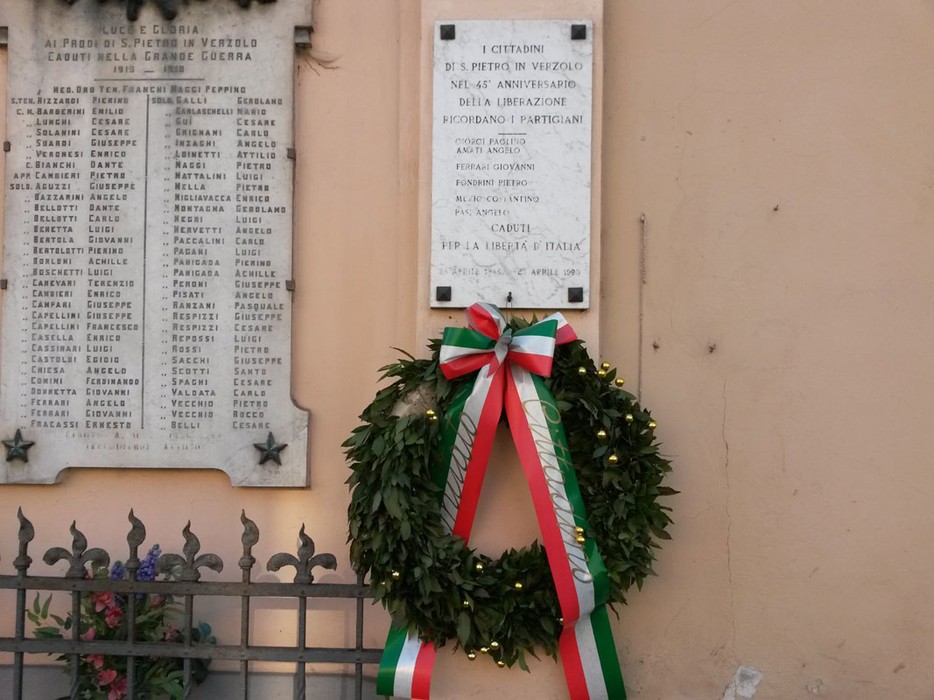 Lapide commemorativa ai caduti partigiani di San Pietro in Verzolo, con corona d'alloro e nastri tricolori.