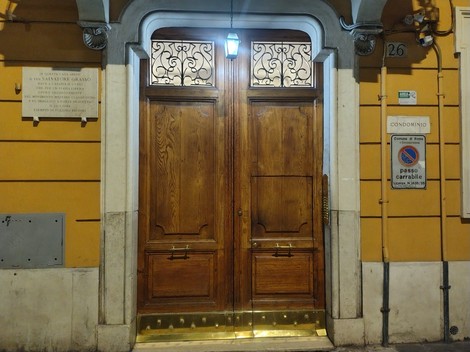 Porta in legno con dettagli decorativi, situata in un ambiente urbano, con illuminazione soffusa e pareti gialle.