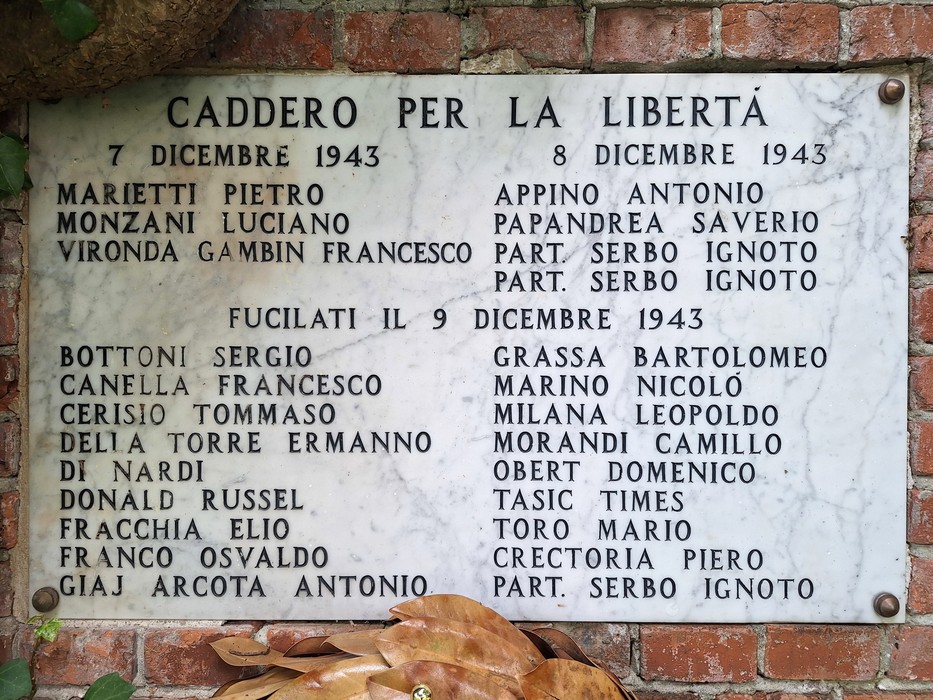 Lapide in marmo con lunga iscrizione a più colonne, fissata su una parete di mattoni a vista.
