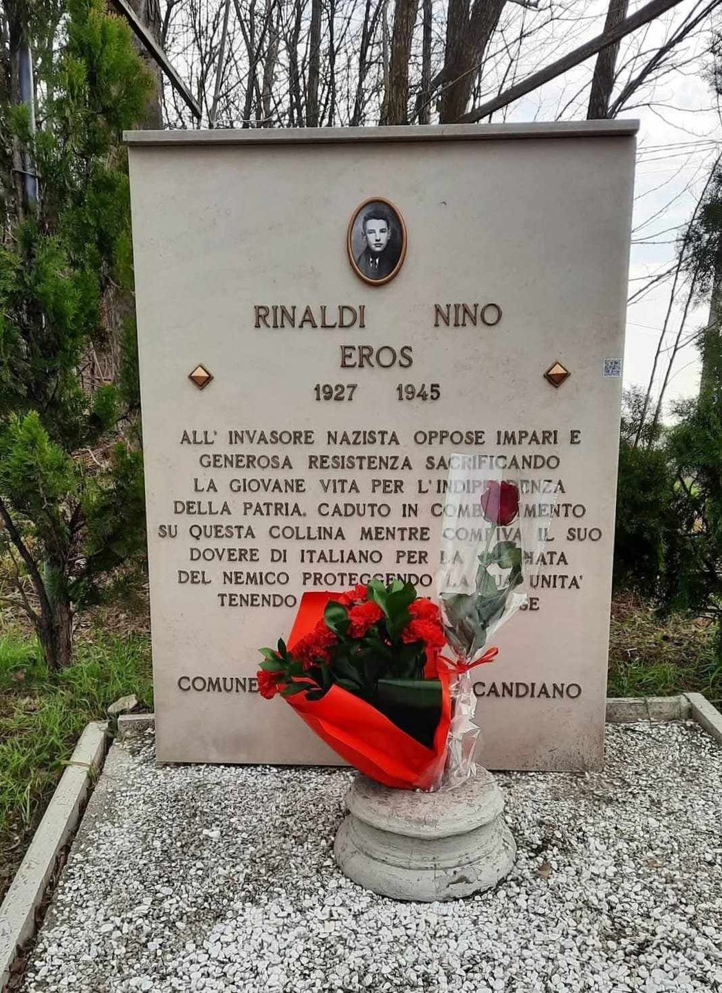 Monumento a Rinaldi Eros, giovane eroe caduto per la libertà, con fiori e segni di rispetto.