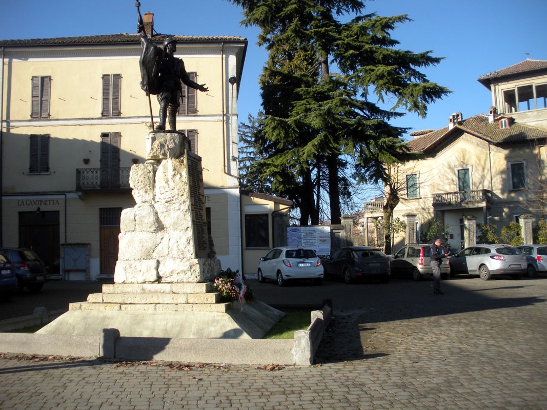 Monumento ai caduti di Mornico Losana in una piazza con edifici e alberi sullo sfondo.
