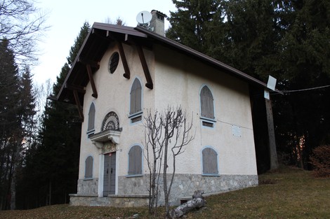 Edificio storico con facciata chiara, finestre con persiane, immerso nella natura circostante.