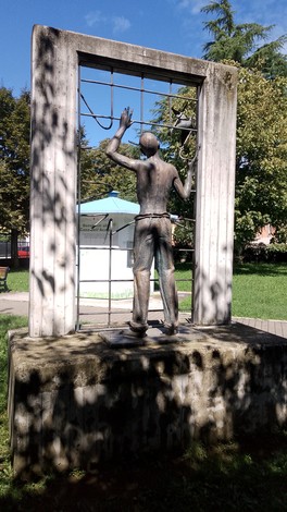 Monumento ai deportati, statua in bronzo che rappresenta un uomo che guarda oltre una rete, simbolo di libertà e speranza.