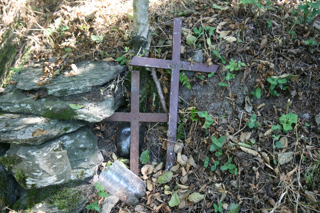 Croci metalliche abbandonate tra foglie e rocce, simbolo di memoria storica e di un passato dimenticato.