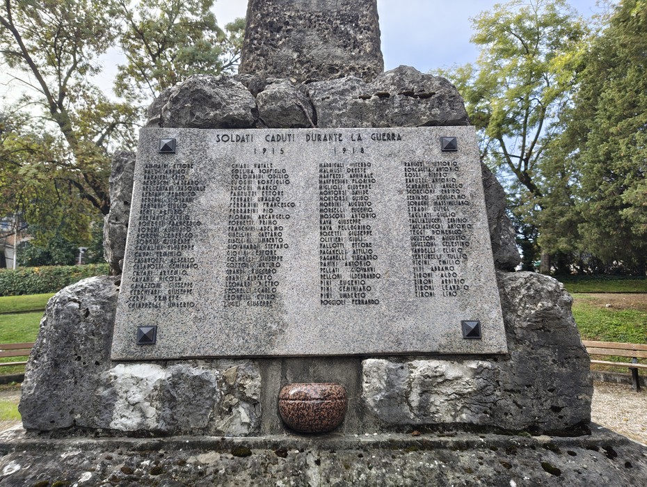 Lastra di pietra con iscrizione e elenco di nomi, incastonata in un monumento di roccia tra gli alberi.