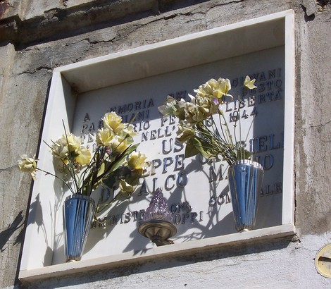 Ossario dei partigiani con fiori bianchi e un'illuminazione, dedicato alla libertà e alla memoria storica.