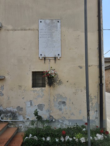 Lapide commemorativa per i caduti per la libertà, affissa su una parete danneggiata, decorata con fiori.