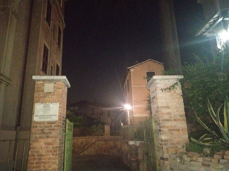 Lapide dedicata a Orlando Lombardi, in un viale illuminato di notte con edifici storici sullo sfondo.