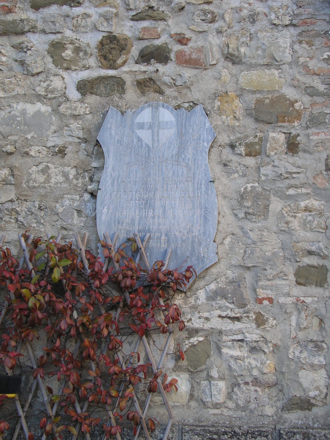 Lapide commemorativa su una parete di pietra, avvolta in piante rampicanti.