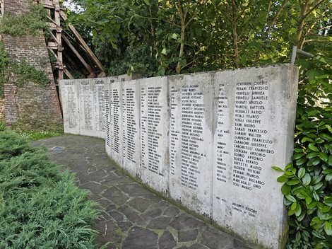 Monumento ai Caduti con elenco di nomi su parete di pietra in contesto verde e tranquillo.