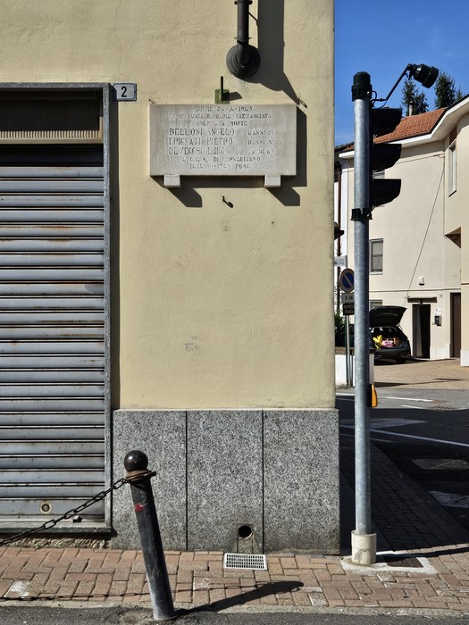 Lapide in marmo con iscrizione, fissata sulla parete di un edificio all'angolo di una strada.
