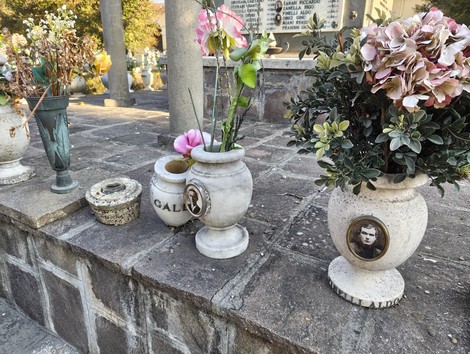 Vasi con fiori e fotografie commemorative in un luogo di memoria dedicato ai caduti.