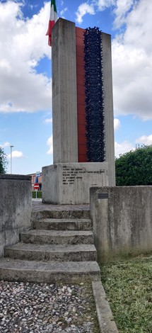 Monumento ai partigiani, una stele in cemento con bandiera italiana, simbolo di memoria storica e resistenza.
