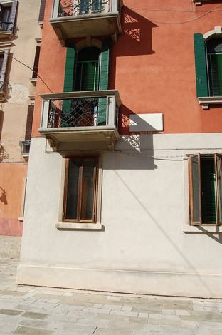 Lapide a Stringari su un muro colorato, con finestre verdi e balcone decorativo, in un contesto urbano.