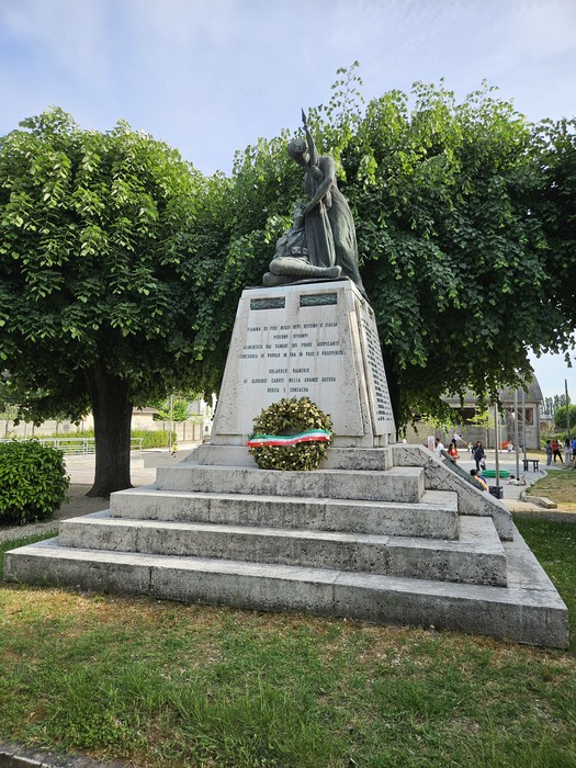 Monumento ai Caduti di Solarolo Rainerio, con una statua su base monumentale, circondato da vegetazione.