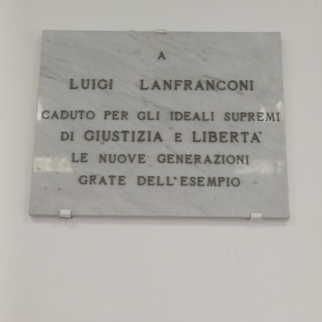 Lapide in marmo bianco con iscrizione dedicata a Luigi Lanfranconi, fissata su parete chiara.