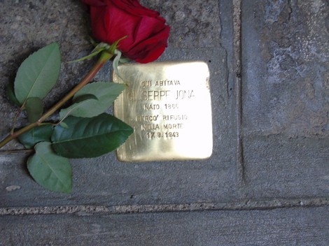 Pietra d'inciampo dedicata a Giuseppe Jona, con rosa e foglie adagiati accanto.