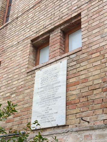 Lapide commemorativa di Lattanzi murata su un edificio in mattoni, con finestre sovrastanti.