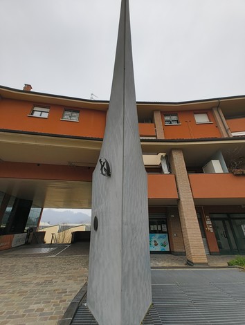 Monumento a Piccinini, struttura di forma slanciata in cemento, situato in un ambiente urbano.