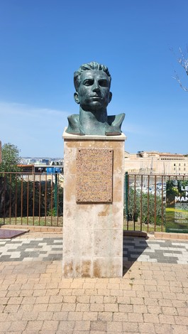 Scultura commemorativa di Missak Manouchian in un giardino, con vista sul paesaggio urbano.