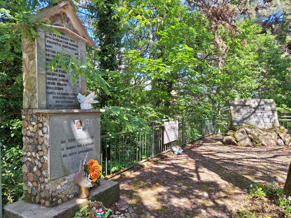 Monumento ai giovani partigiani immerso nel verde, con decorazioni floreali e lapidi commemorative.