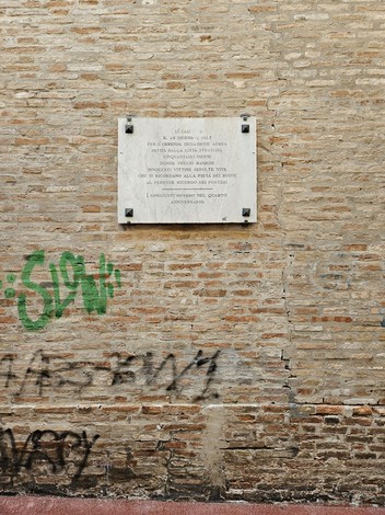 Lapide commemorativa del bombardamento del 28 dicembre 1943 su muro in pietra, con scritte graffiti sottostanti.