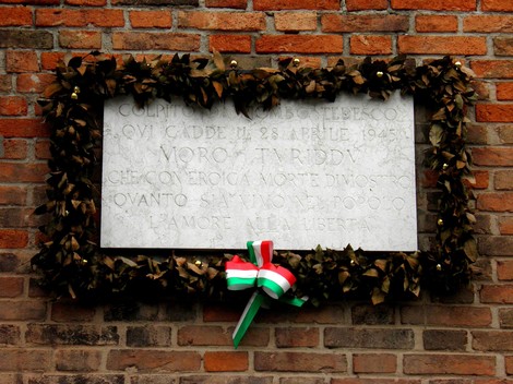 Lapide commemorativa a Moro, decorata con corone di foglie e un nastro tricolore.