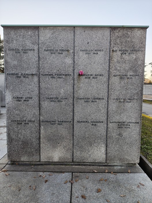 Monumento commemorativo al "Campo della Gloria" con epigrafi di diversi defunti e un fiore posato in tributo.