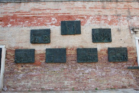 Il Monumento all'Olocausto con varie lastre bronzee su muro di mattoni, simbolo di memoria e riflessione.