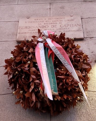 Lapide commemorativa a De Capitani con una corona di alloro e nastri decorativi.