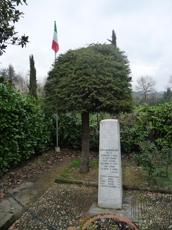Cippo commemorativo ai caduti partigiani di Longuelo, circondato da vegetazione e con bandiera italiana.