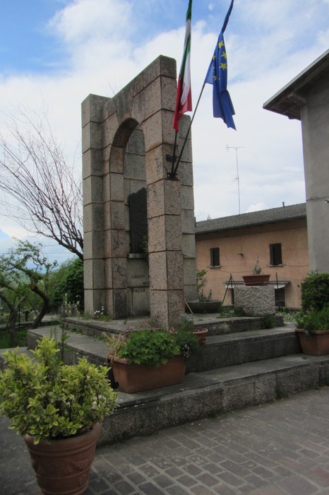 Monumento monumentale dedicato ai caduti della Resistenza, circondato da piante e bandiere.