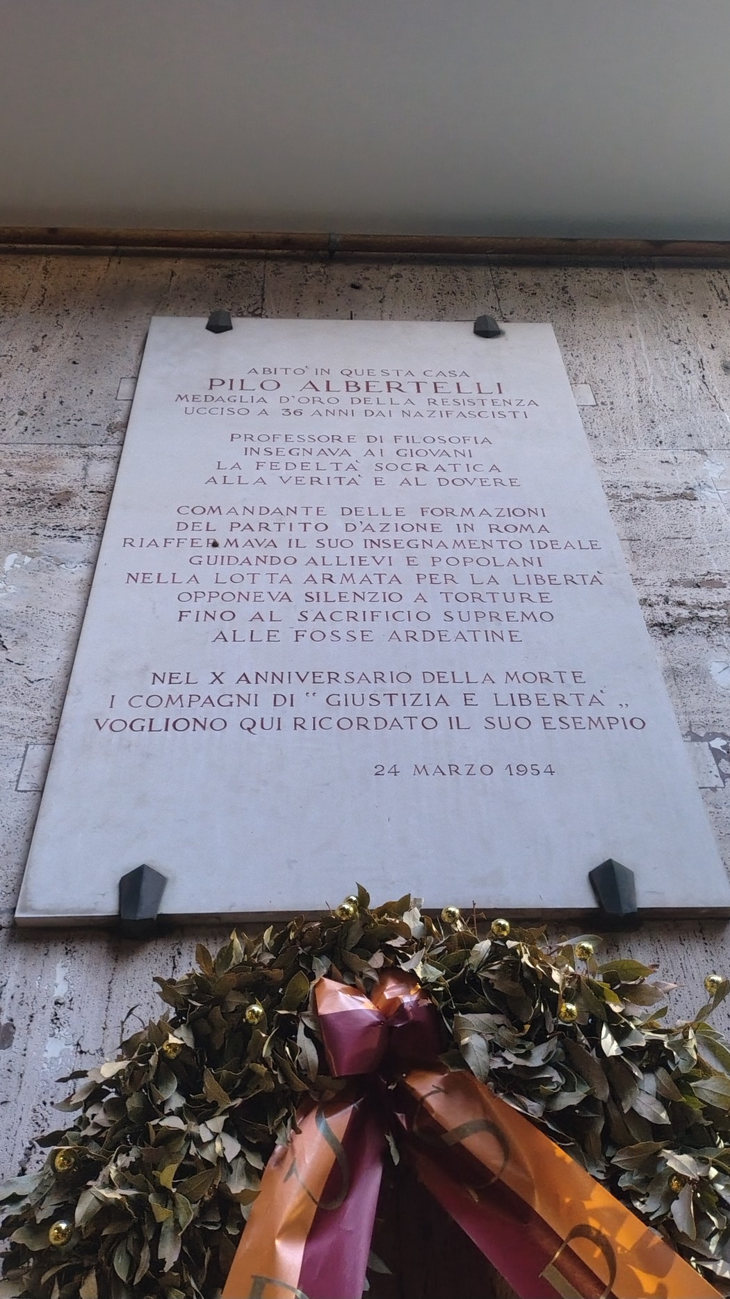 Lapide dedicata a Pino Albertelli, commemorativa di una figura storica, con decorazione floreale e messaggio di ricordo.
