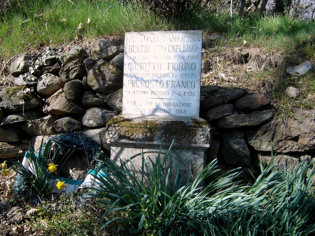 Lapide commemorativa dedicata a Pistono, Enellino, Comotto e Prevosto in un contesto naturale.