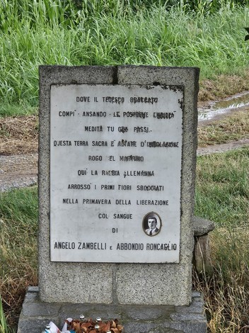 Cippo commemorativo dedicato a Angelo Zambelli e Abbondio Roncaglio, situato in un'area rurale.