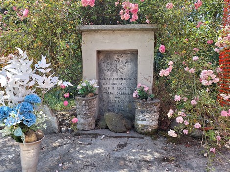 Cippo commemorativo circondato da fiori, dedicato a Farinelli, Fusari e La Rosa, con decorazioni floreali.