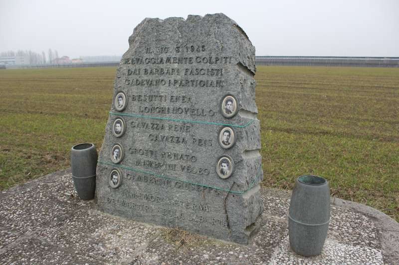 Cippo commemorativo in pietra dedicato a Besutti, Longhi e altri, situato in un campo.