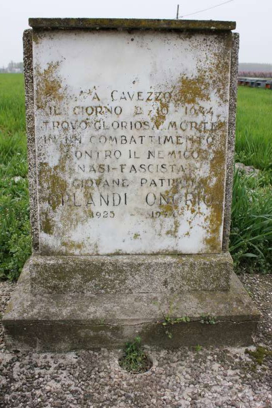 Cippo commemorativo in pietra con iscrizioni, immerso in un paesaggio verde di campagna.