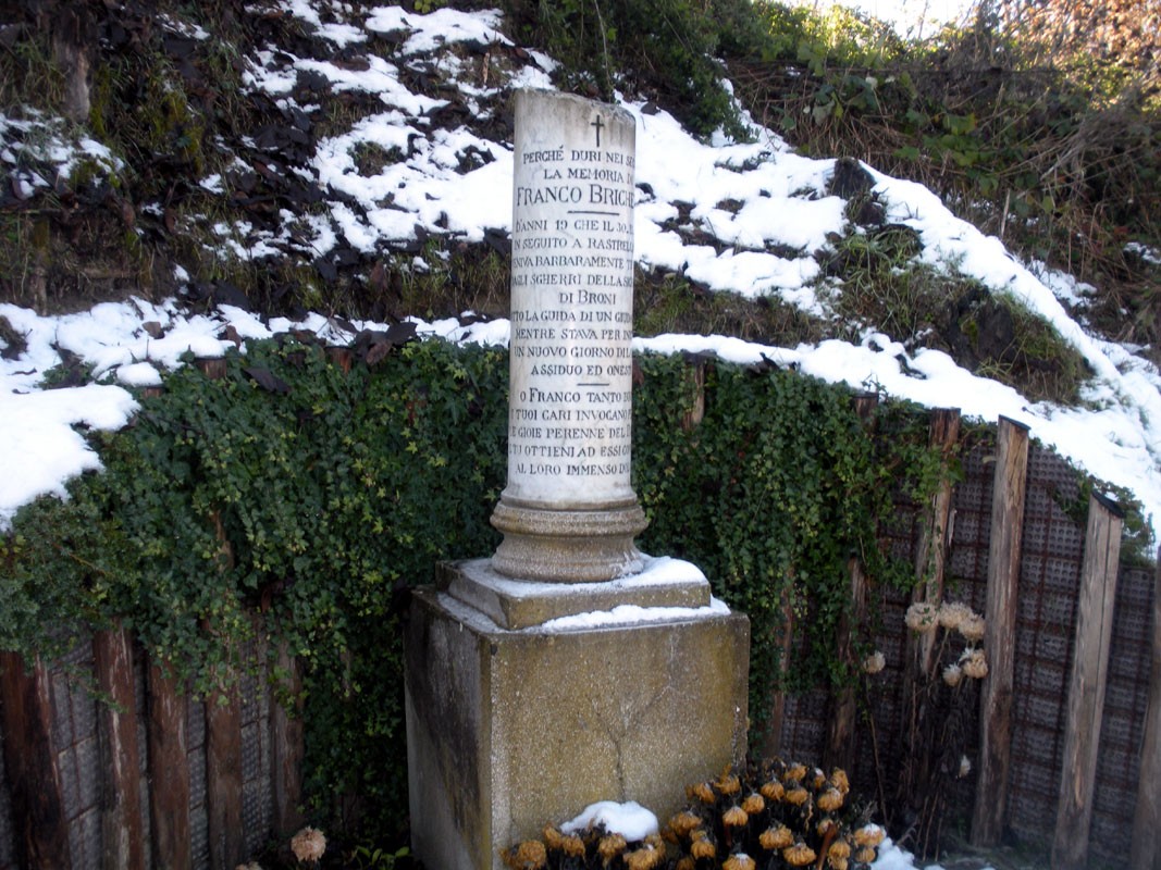 Cippo commemorativo di Franco Brichetti, circondato da neve e vegetazione, situato in un'area rurale.