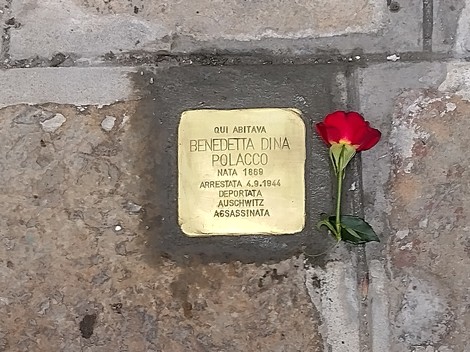 Pietra d'inciampo dedicata a Dina Polacco, con un fiore rosso posato sopra, in memoria della sua storia.