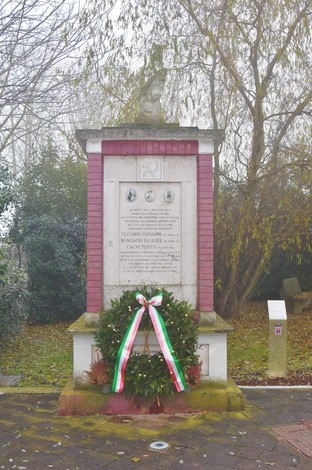 Monumento commemorativo a Zecchini, Bonzagni e Calvi, circondato da vegetazione e decorato con un omaggio floreale.