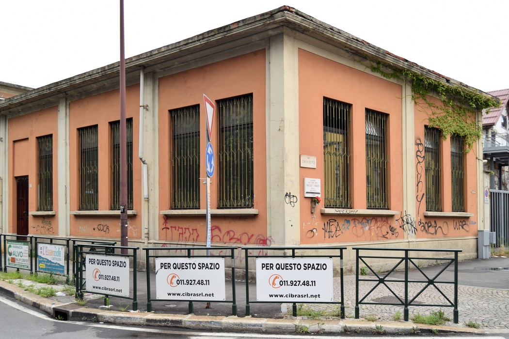 Lapide commemorativa a Prassuit su un edificio con graffiti e recinzione in un contesto urbano.