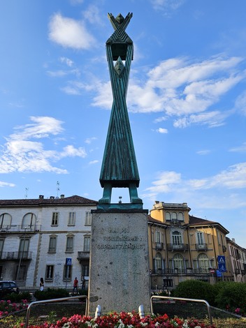 Monumento alla Resistenza con una figura stilizzata e fiori colorati, sullo sfondo di un cielo blu.